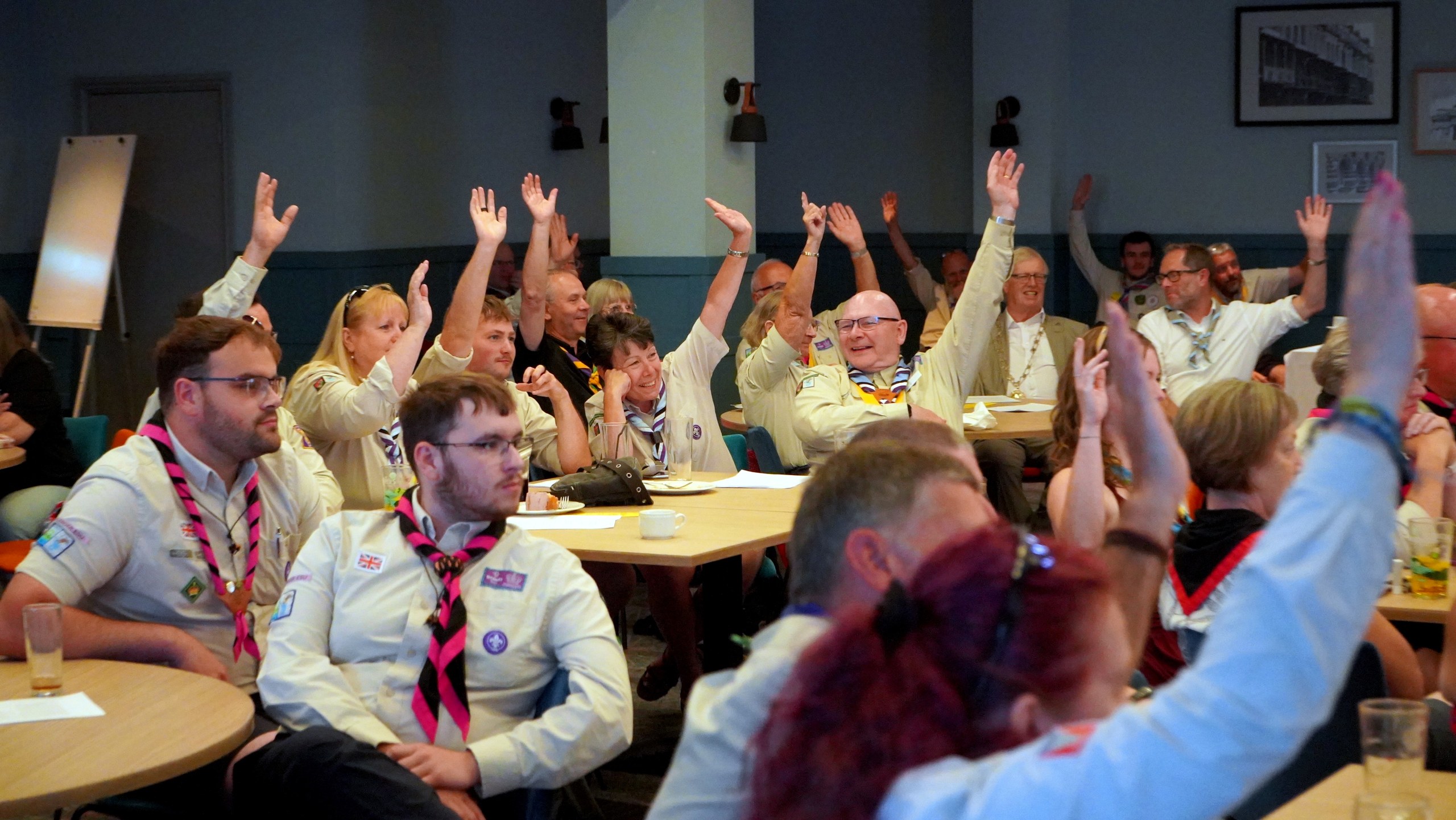 Delegates seated at tables across the hall raise their hands to vote.